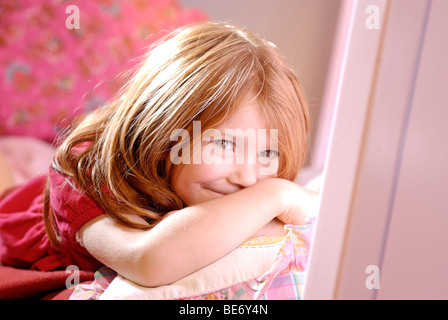 Kleine Mädchen tragen ein romantisches rotes Kleid zwischen die Kissen auf ihrem Bett liegend lächelnd Stockfoto