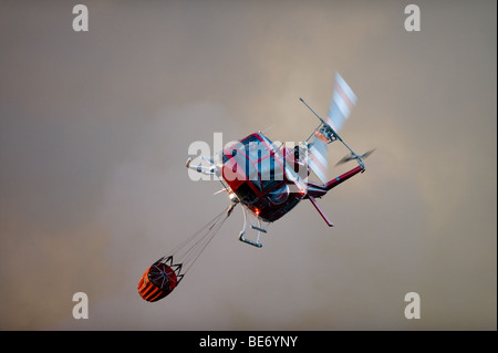 Wasser fallen Hubschrauber kommen, um den Korb mit Wasser aus einem Teich auf einem Golfplatz in der Nähe von Feuer Linien zu füllen. Stockfoto