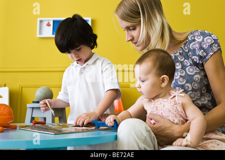 Kleiner Junge arbeiten Puzzle mit Mutter und Säugling Schwester Stockfoto