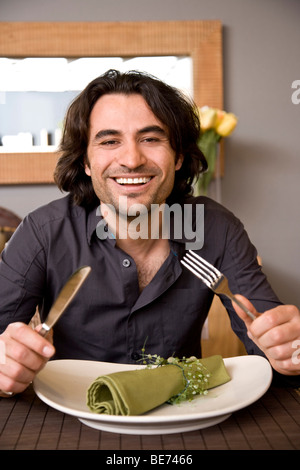 Junger Mann halten Messer und Gabel am Esstisch Stockfoto