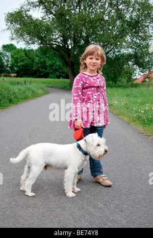 Mädchen, 5, steht auf einem Weg mit einem weißen Zwergschnauzer Stockfoto