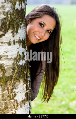 Junge Frau, 20, peering hinter einem Baum Stockfoto