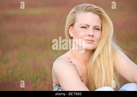 Junge blonde Frau sitzt auf einer Wiese Stockfoto