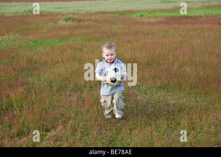 Zwei-jähriger Junge mit einem Ball, über eine Wiese laufen Stockfoto