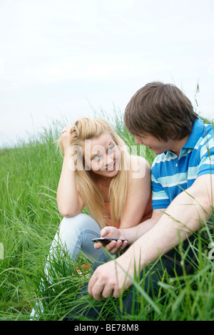 Junges Paar sitzt auf einer Wiese, SMS-Versand Stockfoto