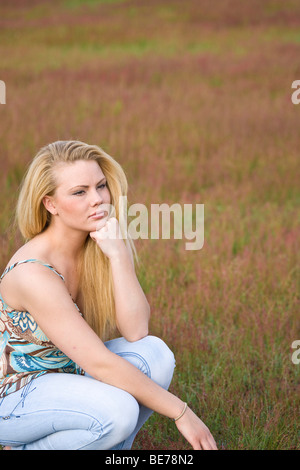 Junge blonde Frau sitzt auf einer Wiese hocken, Blick in die Ferne Stockfoto