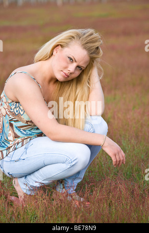 Junge blonde Frau sitzt auf einer Wiese hocken Stockfoto