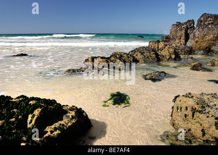 Wellen von einem kristallklaren Meer waschen über Felsen an einem Sandstrand Stockfoto
