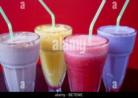 Vier coole Milchshakes gegen eine bunte Wand. Aromen sind Schokolade, Mango, Himbeeren und Heidelbeeren. Stockfoto