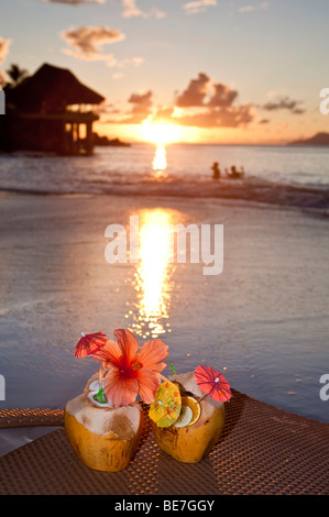 Zwei Kokosnüsse mit Cocktails und Dekorationen, stehend auf einem Liegestuhl bei Sonnenuntergang, in den Rücken der Sunset Beach Hotel, Seychellen, Stockfoto