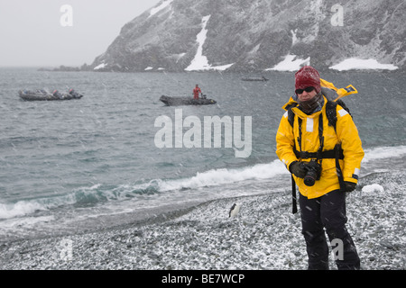 Kaltbearbeitung professioneller Fotograf mit der Kamera stehend auf felsigen Strand in windigen Schneegestöber Sturm in der Antarktis Stockfoto