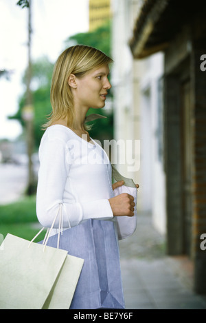 Frau, die Einkaufstaschen auf Arm Fenster shopping, seitliche Ansicht Stockfoto