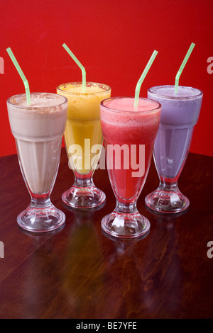 Vier coole Milchshakes gegen eine bunte Wand. Aromen sind Schokolade, Mango, Himbeeren und Heidelbeeren. Stockfoto