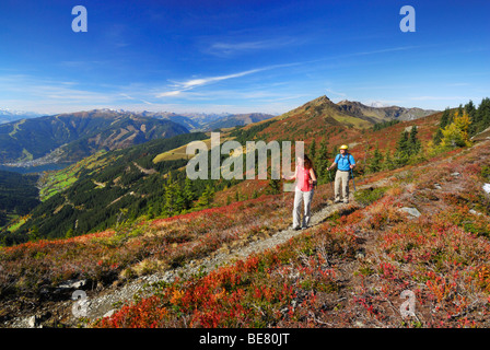 Paar Wandern auf Spuren am Hundstein mit Blick zum Dorf Zell am See, Schmittenhöhe und Schwalbenwand mit herbstlichen Farben der hu Stockfoto