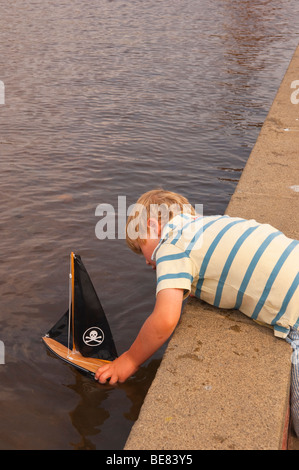 Ein kleiner Junge (Modell freigegeben) Segeln sein Spielzeugboot am Bootfahren See in Aldeburgh, Suffolk, Uk Stockfoto