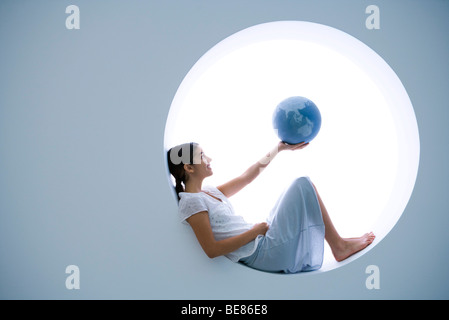 Junge Frau liegend auf der Fensterbank, Globus holding Stockfoto