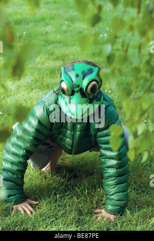 Person mit Frosch Maske, hocken auf Rasen Stockfoto