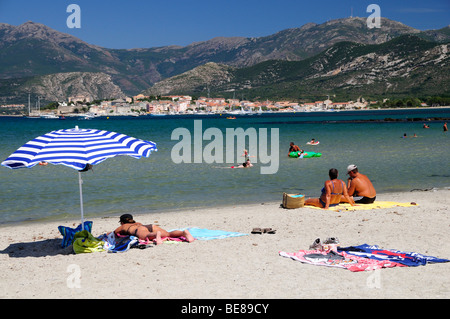 Frankreich Korsika St Florent People auf sandigen Strand und Baden im Mittelmeer mit der Altstadt am Fuße der Berge Stockfoto