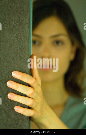 Junge Frau hält sich an die Wand, auf der Suche um Ecke Stockfoto