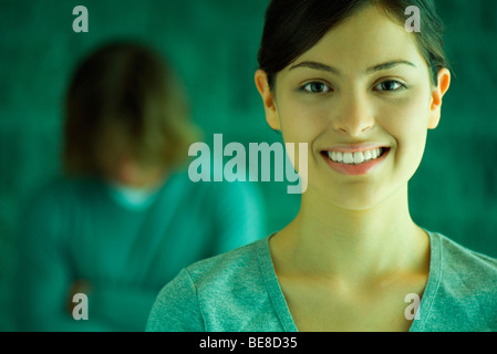 Frau, Lächeln, Mann im Hintergrund mit Kopf gesenkt Stockfoto