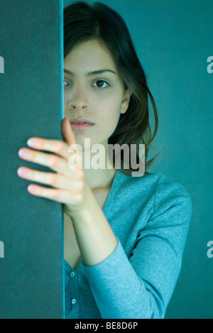 Junge Frau hinter der Wand, um die Ecke in die Kamera schauen Stockfoto