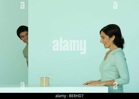 Frau überrascht, Geschenk auf Theke, erwachsener Sohn um Ecke spähen Stockfoto