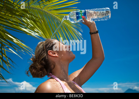 Junge Frau am Strand gießt Wasser aus einer Flasche Wasser über den Kopf, Indonesien, Süd-Ost Asien Stockfoto