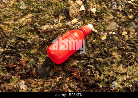 Rote Plastikflasche und Müll, der am Strand aufgespült wurde Stockfoto