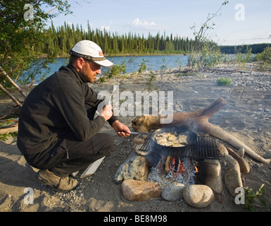 Mann, Kochen, braten Filets in einer Pfanne auf einem Lagerfeuer, oben Liard River, Yukon Territorium, Kanada Stockfoto