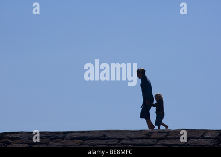 Silhouette eines Mannes und kleine Mädchen zu Fuß entlang einer Ufermauer. Stockfoto