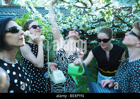 Gruppe von Frauen im Garten, telefonieren, mit Laptop-Computer, Seifenblasen Stockfoto