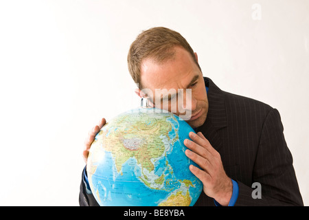 Mann in einem Anzug, lehnte seinen Kopf auf einem Globus Stockfoto