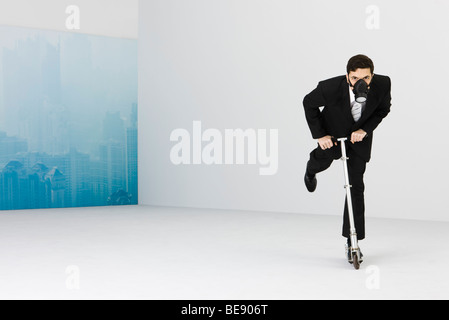 Geschäftsmann, tragen Gasmaske Reiten Push Scooter, Stadtbild von Smog im Hintergrund verdeckt Stockfoto