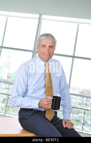 Geschäftsmann, sitzen auf Ecke seines Schreibtisches mit Kaffee-Haferl Stockfoto