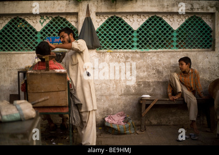 Ein Barbier rasiert eine Mann auf der Straße in Nizamuddin, New Delhi, Indien Stockfoto