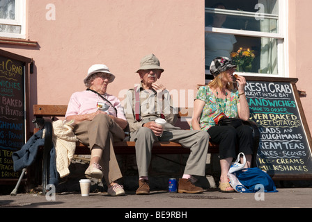 älterer Mann und Frau sitzen auf Bank im Sonnenschein Essen Stockfoto