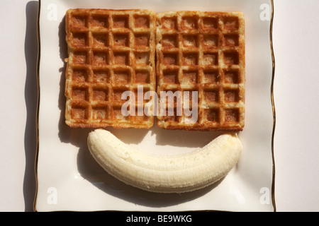 Geschälte Banane mit zwei Waffeln auf weißen Teller set-Konzept der Smiley mit zwei Augen und einem Lächeln auf weißem Hintergrund Stockfoto