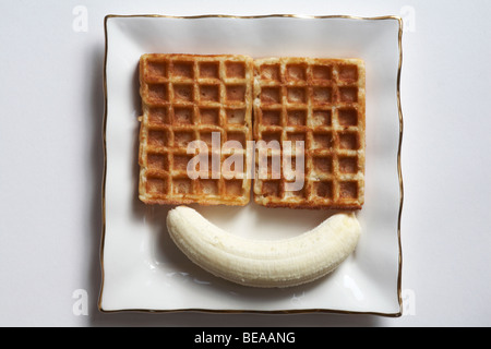 Geschälte Banane mit zwei Waffeln auf weißen Teller set-Konzept der Smiley mit zwei Augen und einem Lächeln auf weißem Hintergrund Stockfoto