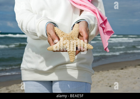 Eine ältere Frau hält einen Seestern am Strand, Mittelteil Stockfoto