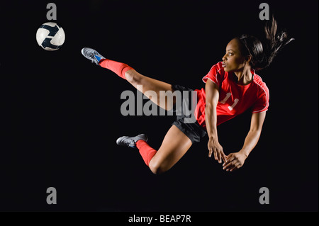 Gemischte Rassen Fußballspieler treten Fußball in der Luft Stockfoto