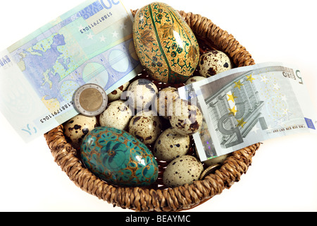 Blick hinunter auf einen Korb mit Eiern - Wachteln und künstlich - und Euro-Banknoten und Münzen. Stockfoto