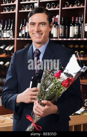 Geschäftsmann hält eine Flasche Weine mit einem Bouquet von Blumen Stockfoto