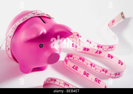 Ein Sparschwein, umwickelt mit einem Maßband in Nahaufnahme Stockfoto