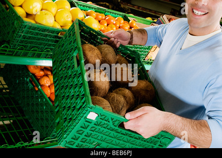 Mann trägt eine Kiste Kokosnüsse in einem Supermarkt Stockfoto