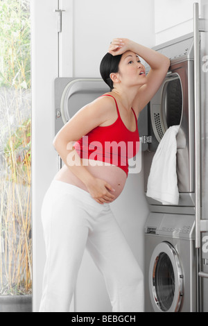 Schwangere Frau sah müde vor einer Waschmaschine Stockfoto