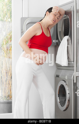 Schwangere Frau sah müde vor einer Waschmaschine Stockfoto