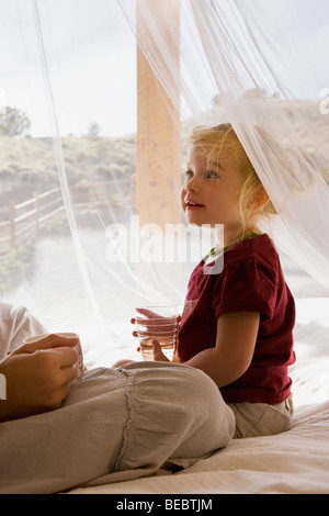 Babymädchen hält ein Glas Wasser und sitzt mit ihrer Mutter Stockfoto