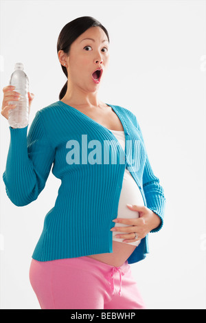 Schwangere Frau auf der Suche nach schockiert und hält eine Flasche Wasser Stockfoto