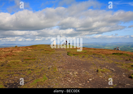 Wanderer mit Hunden an der Trig point ruht auf dem Gipfel des Pendle Hill auf der Pendle, Pendle, Lancashire, England, Großbritannien. Stockfoto