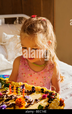 Babymädchen sitzt auf dem Bett mit einer Geburtstagstorte Stockfoto